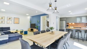 Un soggiorno moderno con divano, tavolo da pranzo e sedie, una cucina con sgabelli da bar e una scala che conduce a un altro piano.