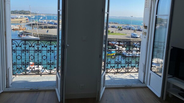 Um quarto com duas portas abertas para uma varanda com vista para uma marina e o mar.