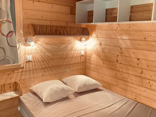Une chambre dans un chalet en bois, avec un lit, deux oreillers et des lampes fixées au mur.