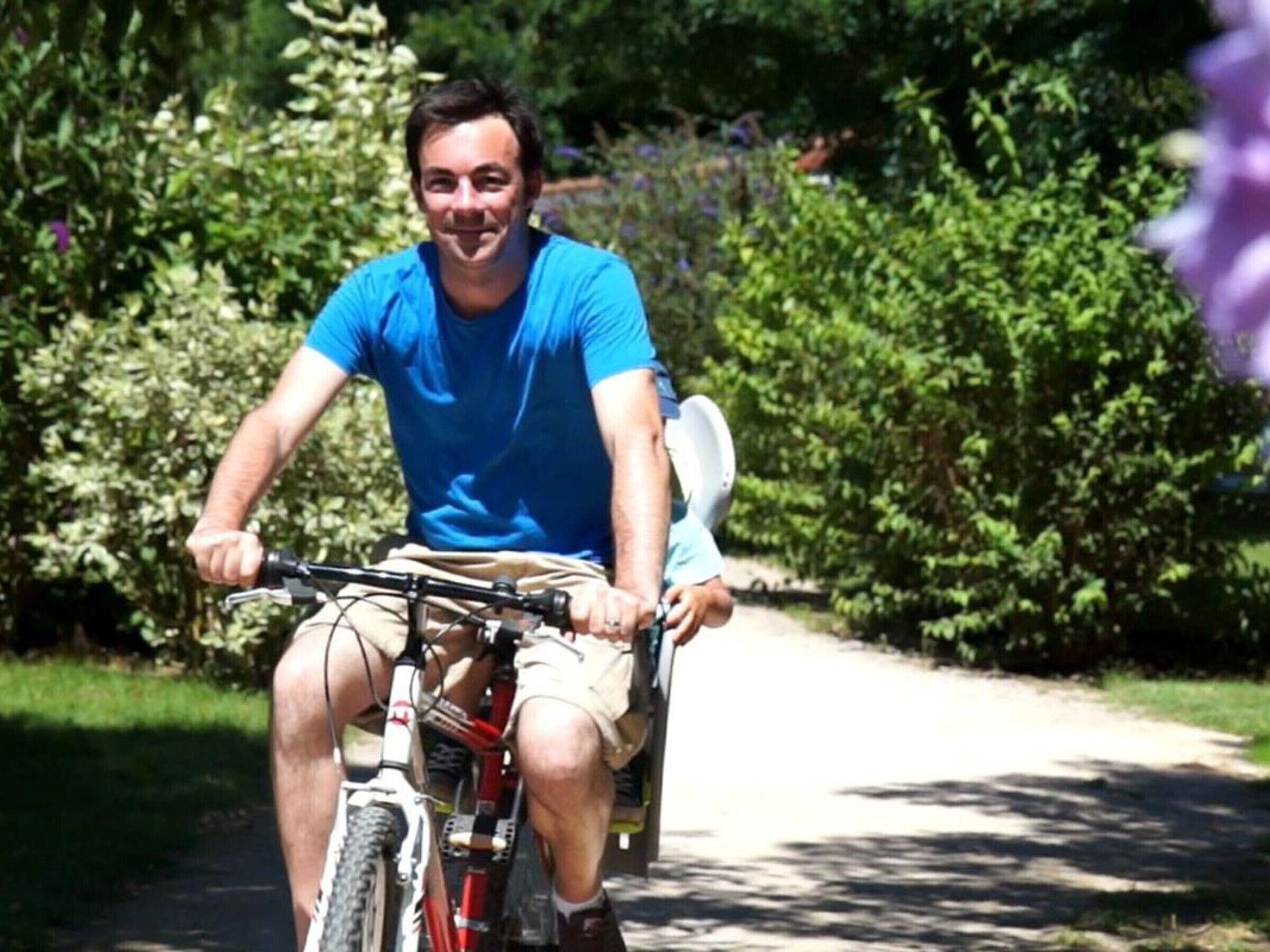 Una persona montando en bicicleta por un camino pavimentado rodeado de vegetación.
