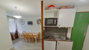 A compact kitchen with a microwave, sink, and a small refrigerator. There is a dining table with chairs and a clock on the wall. - Apartment in Les Rousses with Terrace (Les Rousses)