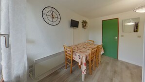 A dining area with a table, chairs, a clock, a TV, and a green door. - Apartment in Les Rousses with Terrace (Les Rousses)