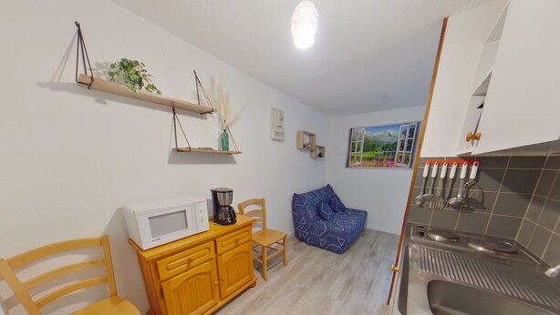 A compact kitchen with a microwave, coffee maker, and a sink. There is a wooden cabinet, a blue bean bag chair, and a small window with a view of greenery. - Apartment in Les Rousses with Terrace (Les Rousses)