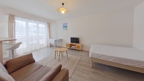 A modern, well-lit room with a sofa, a bed, a desk, and a television. - Spacious Studio, Quiet and Central (Les Rousses)