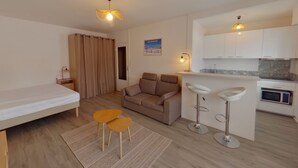 A compact living space with a bed, sofa, two yellow chairs, a small kitchen area, and a dining table. - Spacious Studio, Quiet and Central (Les Rousses)