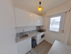 A small, modern kitchen with white cabinets, a stainless steel sink, a microwave, and a window with a view of a snowy landscape.
