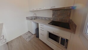 A modern kitchen with white cabinets, a stainless steel sink, a patterned backsplash, and a built-in oven. - Spacious Studio, Quiet and Central (Les Rousses)