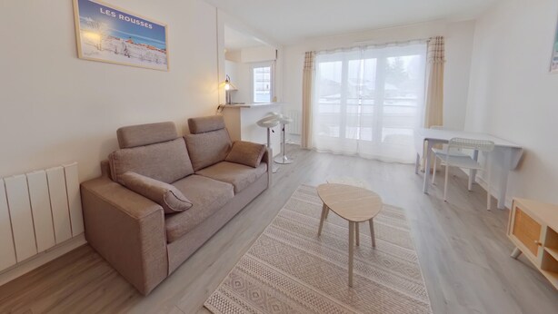 A living room with a sofa, a small round table, a lamp, and a painting on the wall. - Spacious Studio, Quiet and Central (Les Rousses)