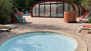 Une piscine circulaire, avec une paroi en verre en arrière-plan, entourée de chaises longues et de plantes en pot.