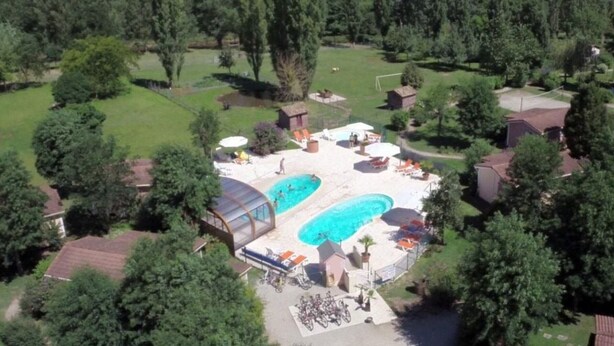 Une vue aérienne d’un complexe hôtelier doté de deux piscines, entouré d’une végétation luxuriante et avec un grand bâtiment en arrière-plan.
