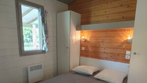 Un lit simple avec deux oreillers, une fenêtre avec des rideaux, une armoire blanche et un plafond en bois.