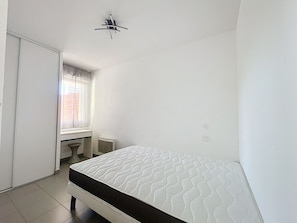 A small, clean room with a single bed, a window with curtains, and a radiator. - Bright 1-Bedroom Apartment in Argelès-sur-Mer (Argelès-sur-Mer)