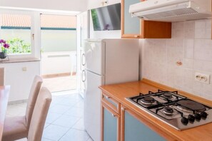 A kitchen with a gas stove, a refrigerator, and a TV mounted above the stove. - Cozy Apartment for 5 near the Sea (Povljana)