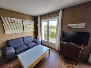 Ein Wohnzimmer mit einer Couch, einem Couchtisch, einem Fernseher auf einem Holzboden und einer Schiebetür zu einem Außenbereich.
