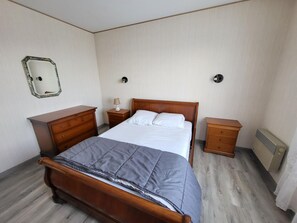 Ein Schlafzimmer mit einem hölzernen Bett, einem Nachttisch mit Lampe, einer Kommode und einem Spiegel an der Wand.
