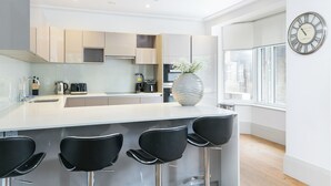 Una cocina moderna con una isla central, taburetes de bar, un jarrón grande y un reloj de pared.