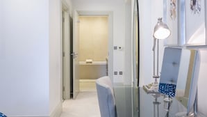 Un baño de hotel con cabina de ducha de vidrio, un perchero y un espejo con una obra de arte encima.