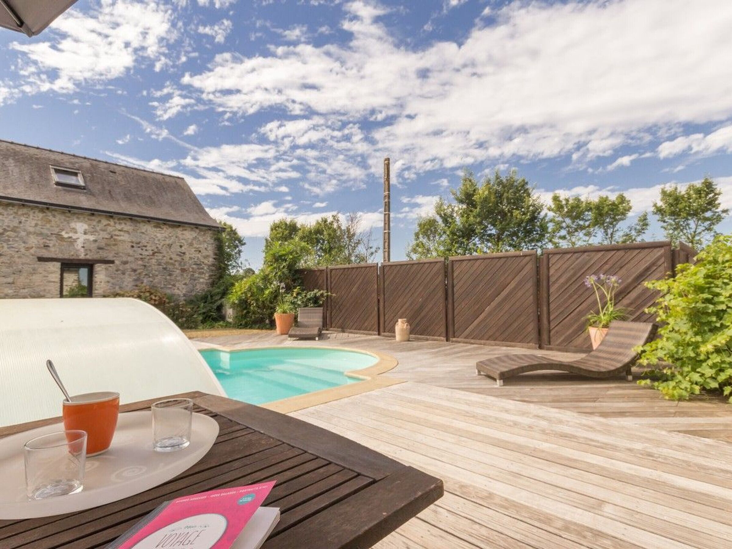 Une terrasse en bois avec une piscine, des chaises longues et une table avec des boissons.