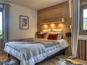 A bedroom with a wooden headboard, a bed with multiple pillows, a framed picture on the wall, and a window with curtains. - 3-Bedroom Apartment, South/West Terrace, Parking - Megève (Megève)