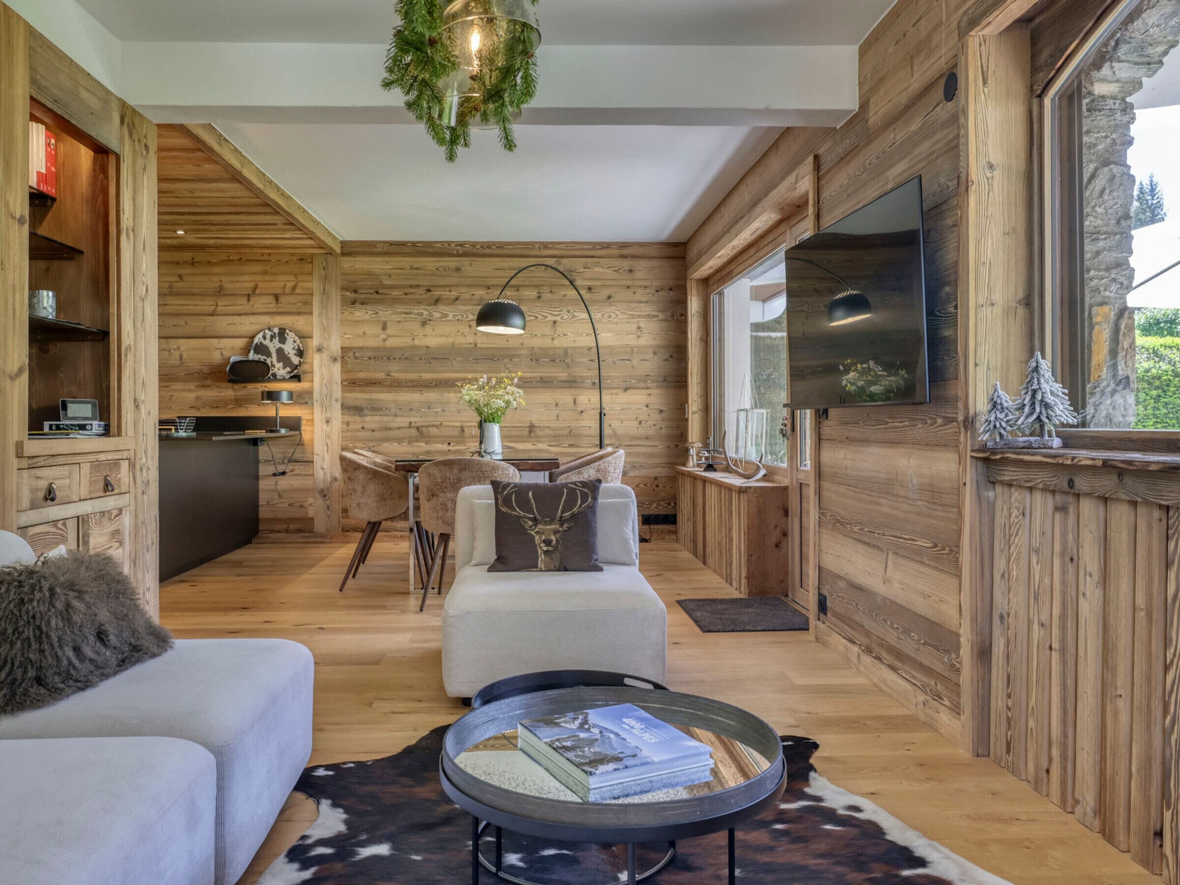 Interior acogedor de una cabaña con detalles de madera, un comedor, un sofá, una mesa de centro y un televisor.