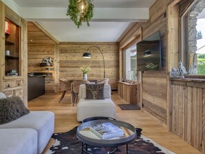 A cozy cabin interior with a wooden interior, a dining area, a sofa, a coffee table, and a television. - 3-Bedroom Apartment, South/West Terrace, Parking - Megève (Megève)