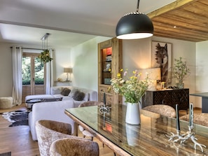 A modern living room with a glass dining table, white sofas, and a wooden ceiling. - 3-Bedroom Apartment, South/West Terrace, Parking - Megève (Megève)