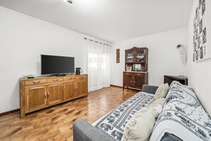 Un salon avec un téléviseur, un meuble en bois, un canapé et un tapis à motifs.