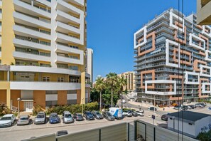 Un parking à plusieurs étages où les voitures sont garées en rangées, à côté d’un immeuble jaune doté de balcons, et un fourgon bleu est visible au premier plan.