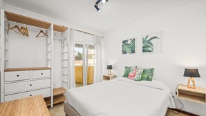 Ein Schlafzimmer mit einem Bett, einem Holztisch, einem Kleiderschrank, einem Nachttisch und einem an der Wand befestigten Regal.