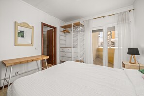 Une chambre à coucher comprenant un lit, un bureau en bois, une armoire et une table de chevet avec une lampe.