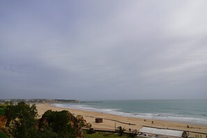 Uma praia com areal, algumas pessoas e um píer ao longe.