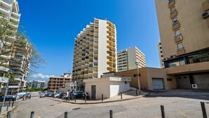 Ein mehrstöckiges Gebäude mit Balkonen, einem Parkplatz und blauem Himmel.