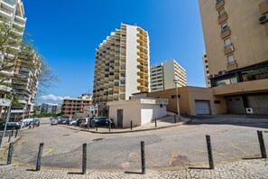 Un immeuble à plusieurs étages doté de balcons, d’un espace de stationnement et surplombant un ciel d’un bleu limpide.