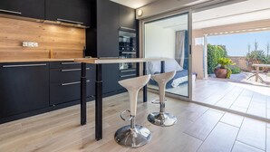 Una cocina moderna con armarios oscuros, encimera de madera y una zona de bar con dos taburetes blancos.