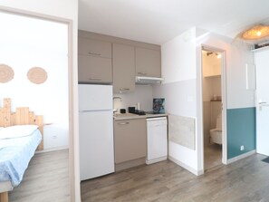 A compact kitchen with a dishwasher, a sink, and a stove. There is a bed with a blue blanket in the adjacent room. - Modern A/C T2 with Pool in Sète (Sète)