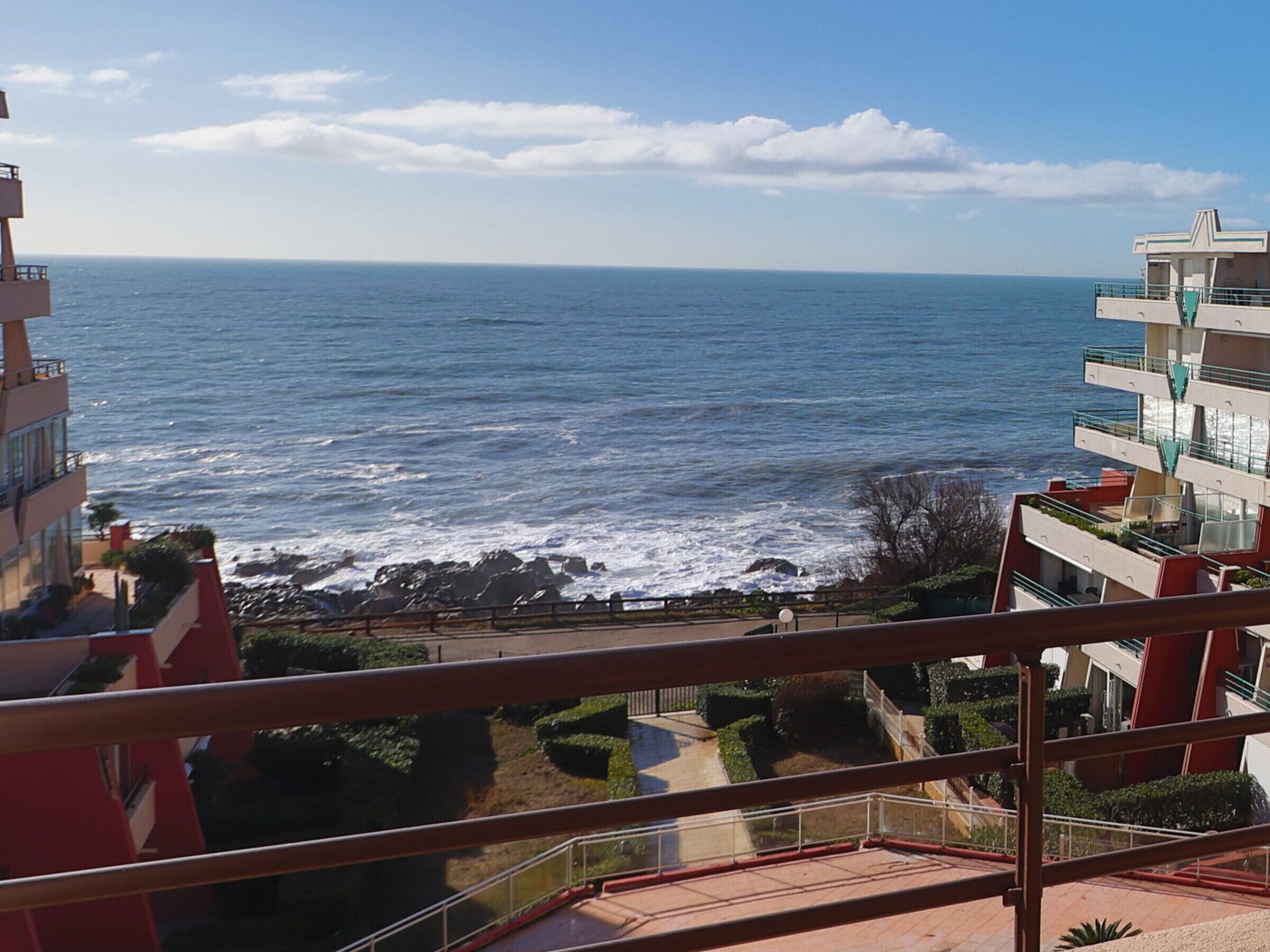 A coastal view from a balcony overlooking the sea, with a promenade and buildings in the foreground.