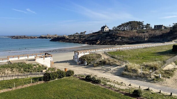 Paisagem costeira com uma praia, uma ponte e uma colina com um edifício.