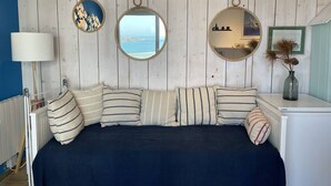 Quarto com cama, almofadas listradas, espelho redondo e vista para o mar.