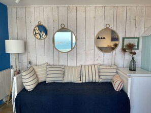 Ein Schlafzimmer mit einem Bett, gestreiften Kissen, einem runden Spiegel und Blick auf das Meer.