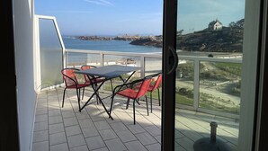 Varanda com mesa e cadeiras, vista para a costa e uma casa numa colina.