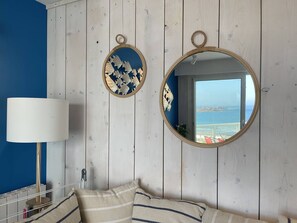 Ein Schlafzimmer mit einem Bett, einem runden Spiegel, einer Lampe und Meerblick durch ein Fenster.