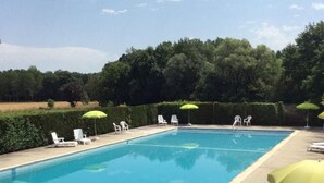 Una piscina rectangular con agua azul cristalina, rodeada de sillones blancos y sombrillas verdes.