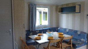 Una habitación compacta con una mesa de comedor y sillas, un banco azul con estampado y una ventana con cortinas.