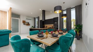 Un espace repas moderne avec des chaises de couleur turquoise, une table en bois dressée avec des assiettes et des verres, et des luminaires suspendus.