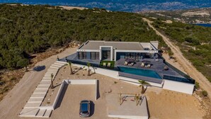 Une villa moderne dotée d’une piscine, d’une voiture garée dans l’allée et offrant une vue sur le paysage environnant.