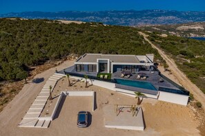 A modern villa with a swimming pool, a car parked in the driveway, and a view of the surrounding landscape.