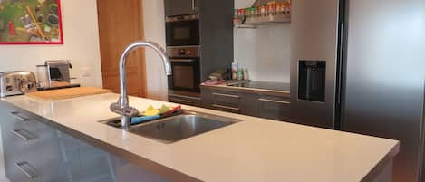 Uma cozinha moderna com eletrodomésticos de aço inoxidável, uma ilha central com pia e armários de madeira.