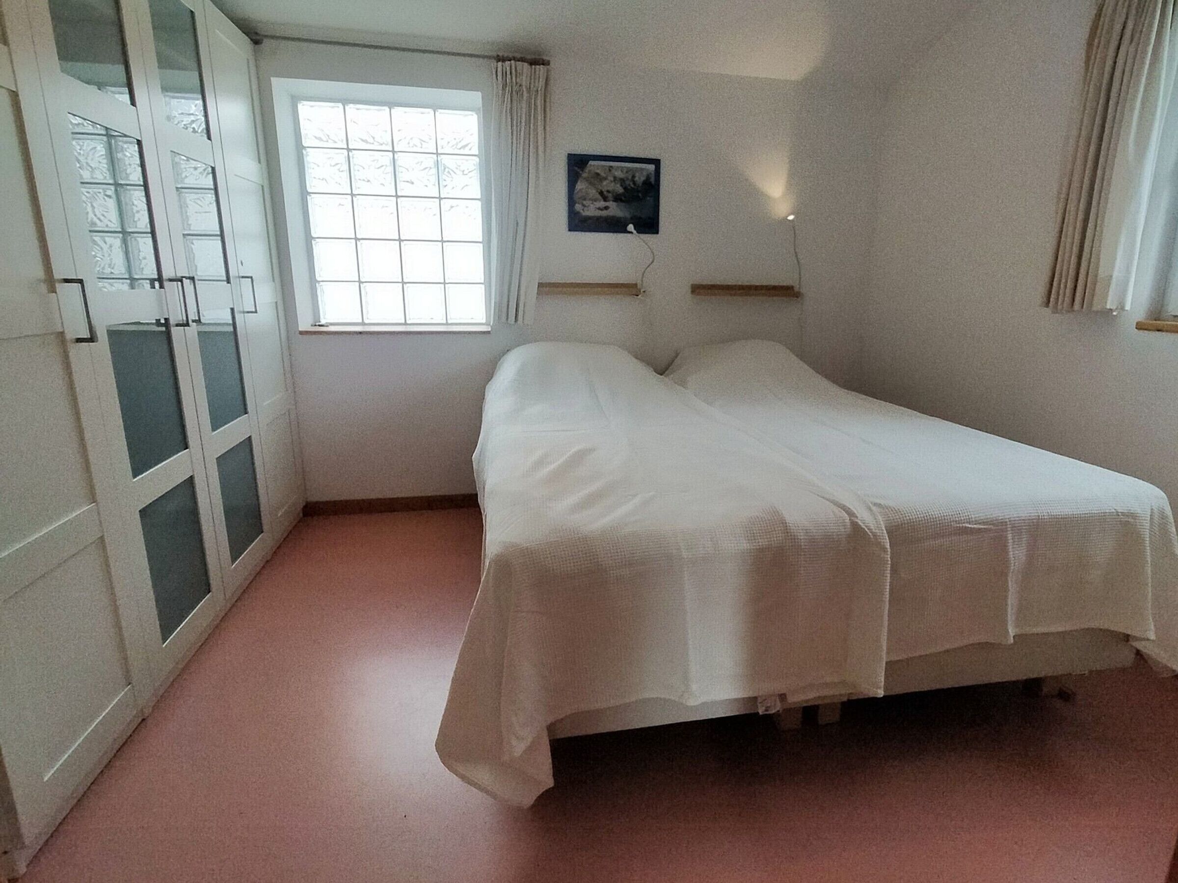 A bedroom with a bed, a window, a painting, and a wardrobe.