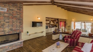 Un amplio salón con chimenea, vigas de madera, televisión y una cocina al fondo.