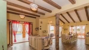 Una cocina amplia con vigas de madera, un comedor con mesa y sillas, y vistas a un patio exterior a través de un ventanal.